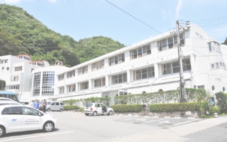 山裾に建つ白い多層介護施設の外観。駐車場と緑地を備える